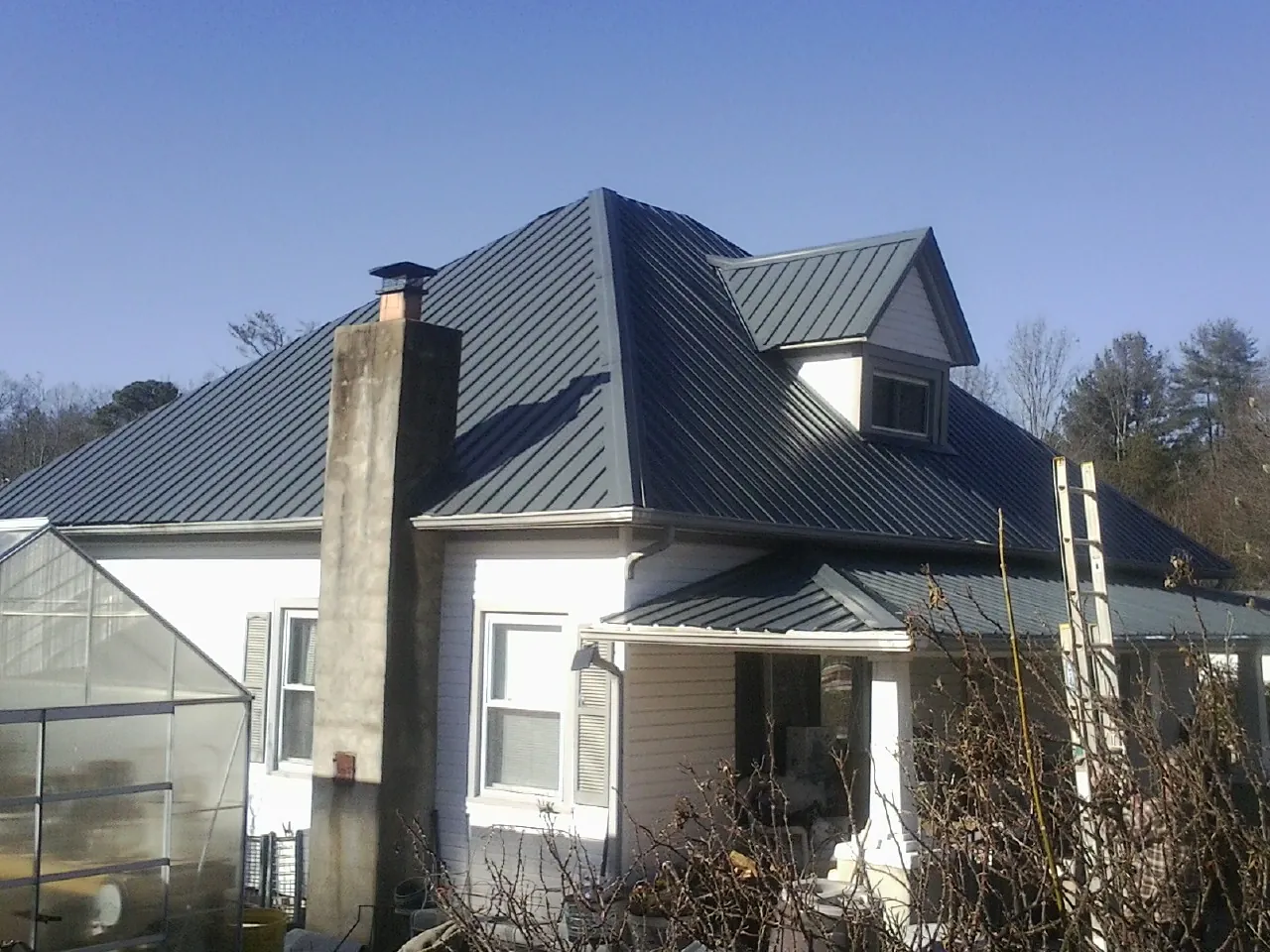 Dark blue standing seam metal roof on a white farmhouse with dormer — Slate & Tile Roof Repair by Roofing Brothers in Enfield