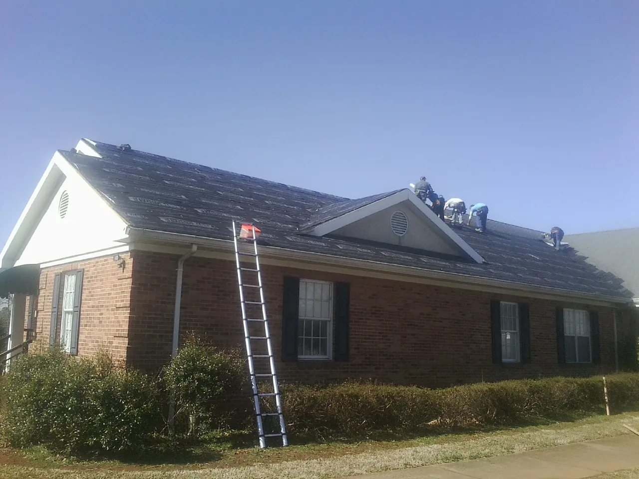 Crew tearing shingles off a brick ranch roof with a ladder set — Metal Roof Repair work by our crew in Enfield