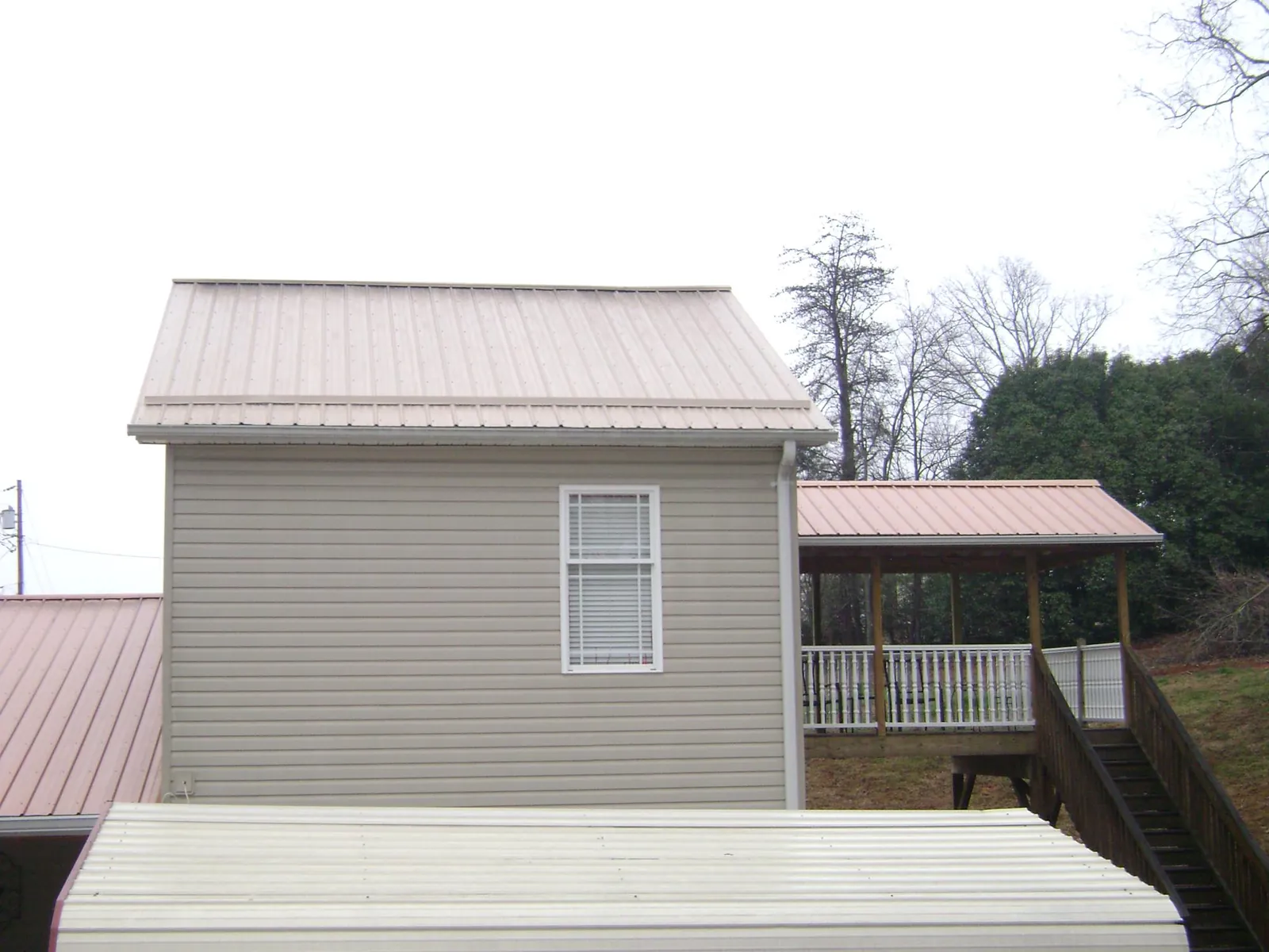 Tan metal roofs on a two story addition and attached porch, from a Roof Replacement job in Enfield